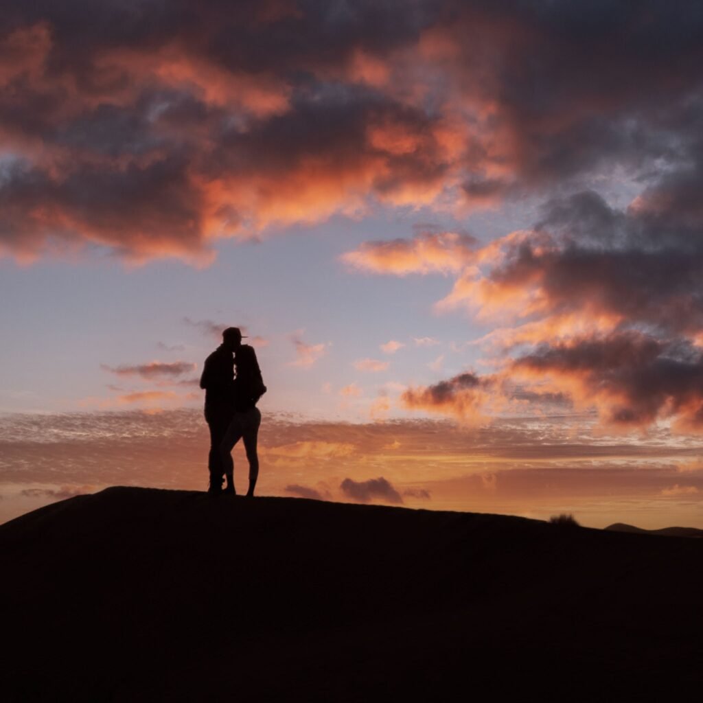 Silhouette of a couple embracing on a hill during a vibrant sunset.